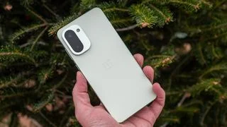 Holding a mint green OnePlus 15R in front of a pine tree