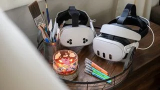 A Meta Quest 3 and Meta Quest 3S alongside a candle, can of paintbrushes, and five markers
