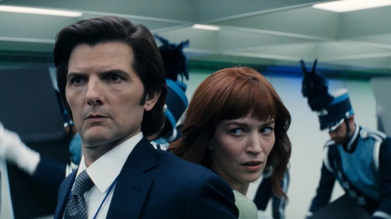 Standing back to back, Severance's Mark Scout and Helly R look at a marching band parading around the office with looks of shock.