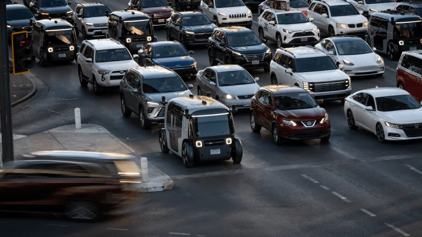 Three Zoox robotaxis wait in traffic among other cabs and private vehicles.