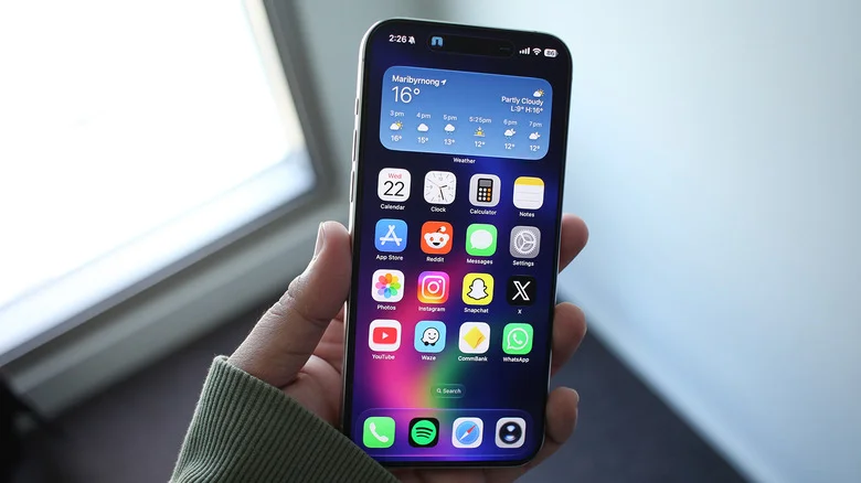 Person holding an iPhone displaying the home screen.