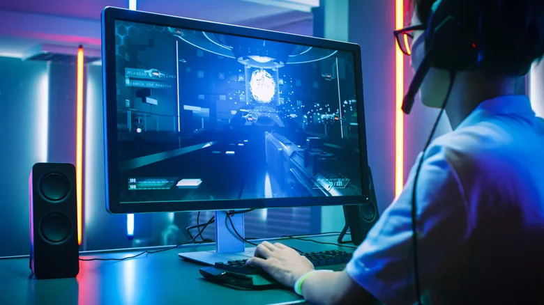 A gamer playing a first-person shooter on a PC monitor.