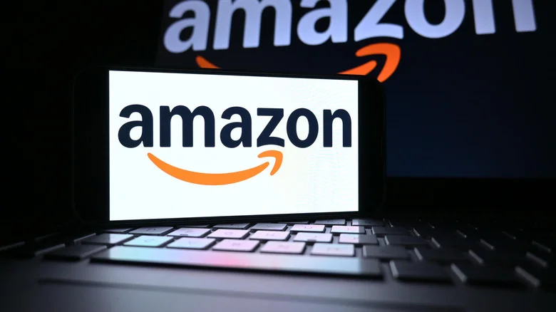 Phone screen displaying the Amazon logo with an open laptop displaying the same in the background.